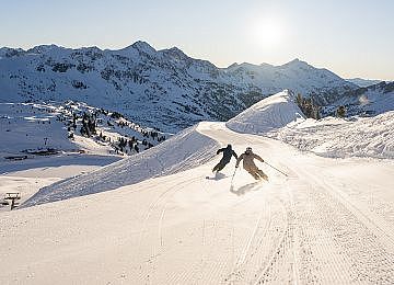 Zwei Skifahrer fahren bei Sonnenaufgang die Piste in Obertauern hinunter.